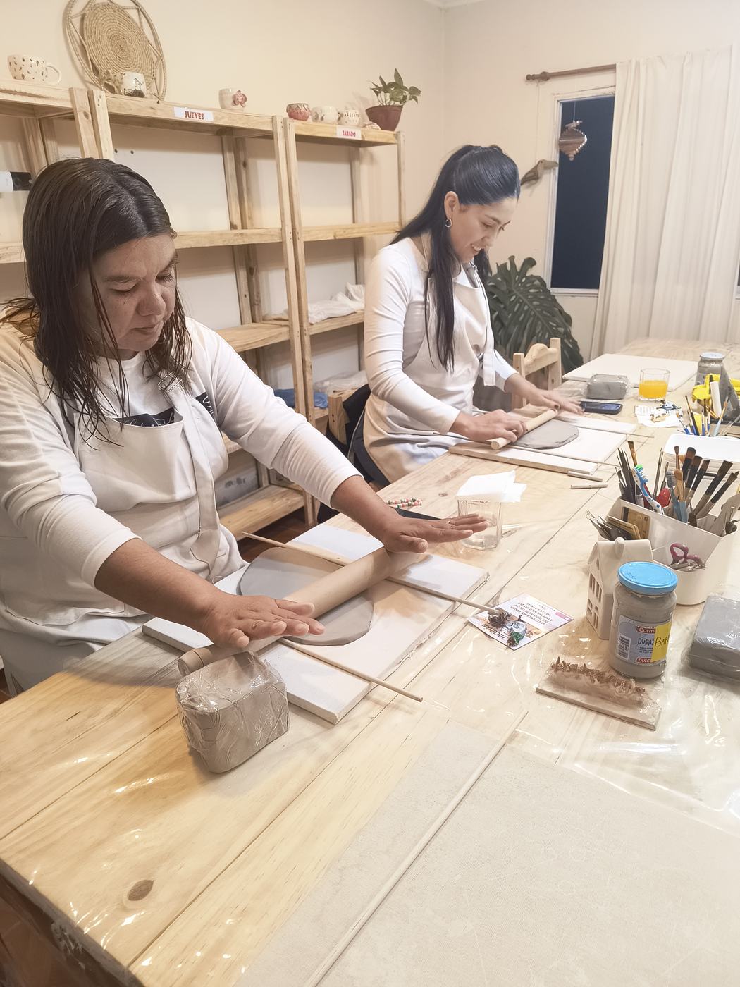 Dos alumnas modelando arcilla en la mesa larga del taller
